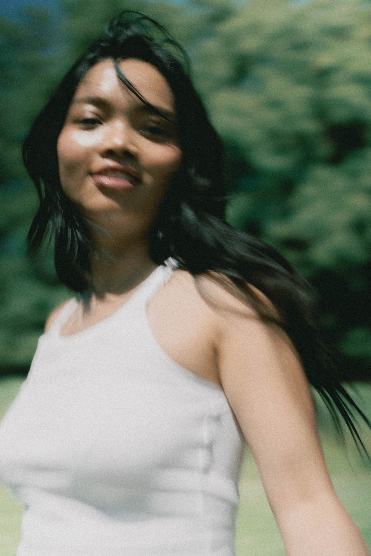 Woman in a white sleeveless top outdoors against soft green foliage