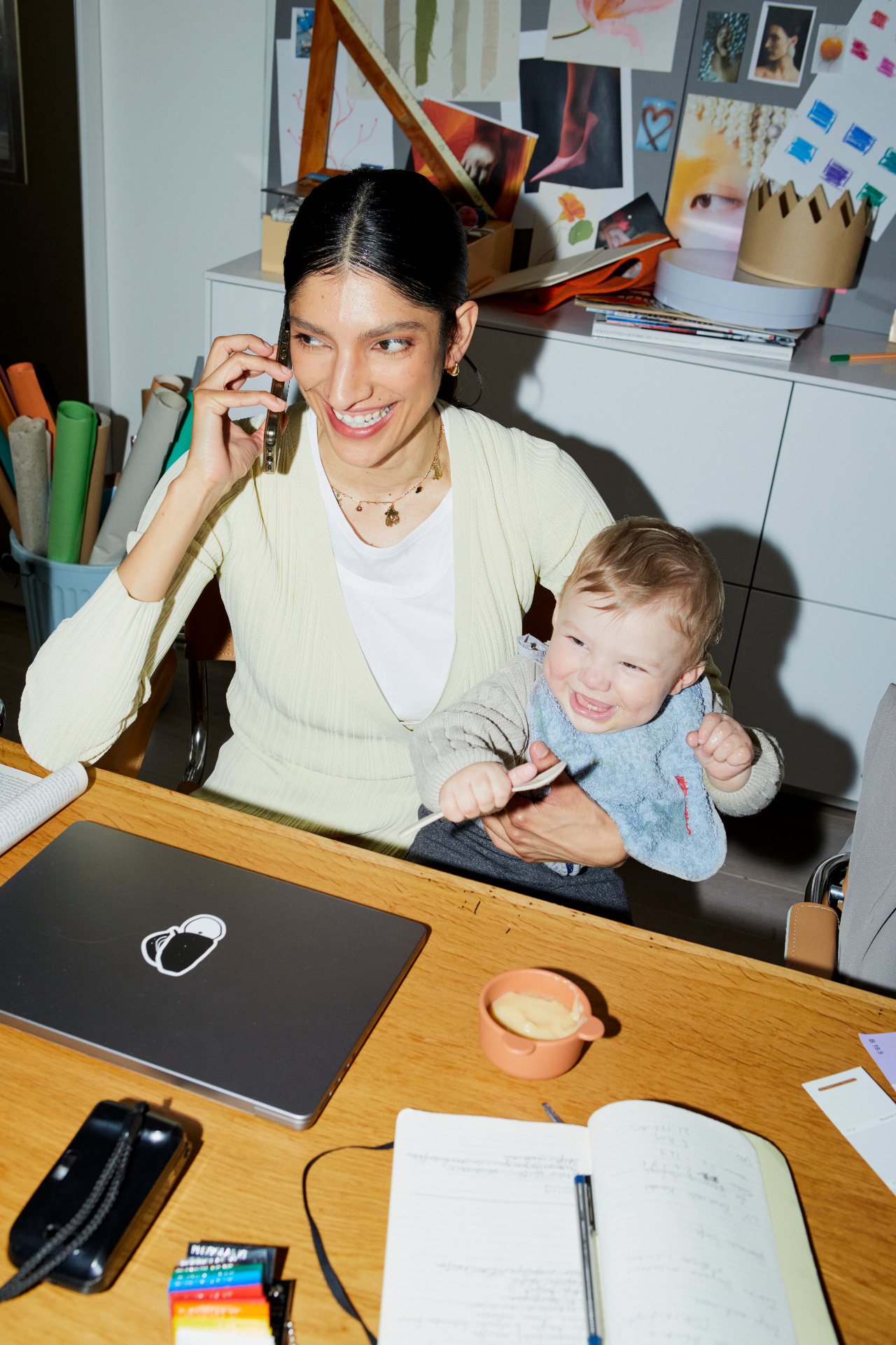 Woman working at a desk while talking on the phone and holding her smiling baby